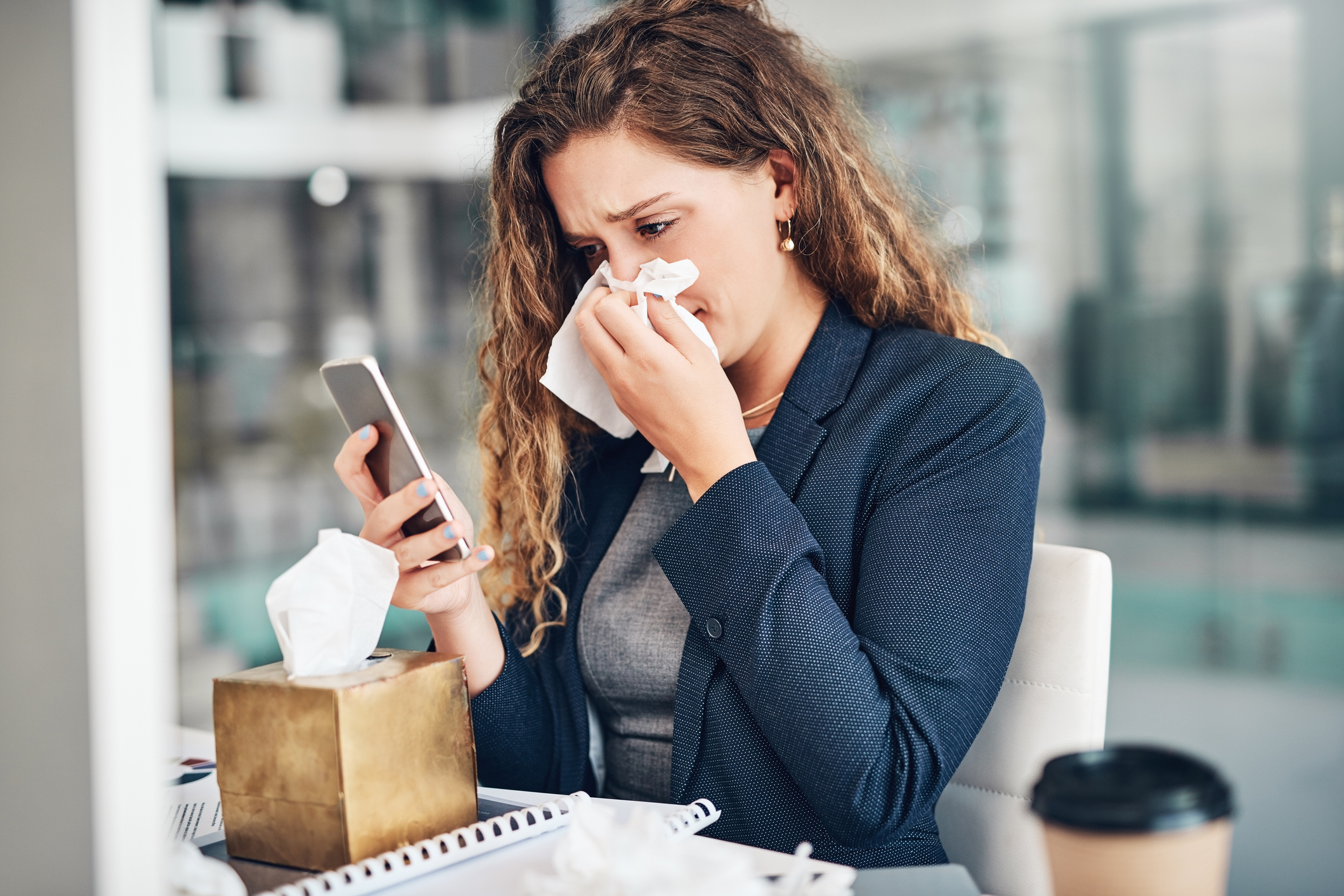 Eine Frau hält sich ein Taschentuch an die Nase und schaut auf ihr Handy