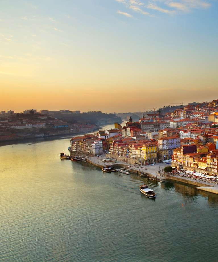 Man sieht einen Hügel mit der Altstadt von Porto. Im Vordergrund ist ein Fluss zu sehen.