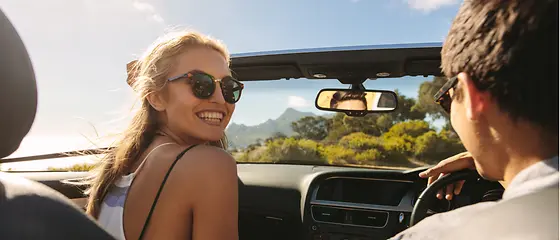 Ein Pärchen sitzt im Cabrio und genießt die Sonne. Die Frau lächelt in die Kamera. 