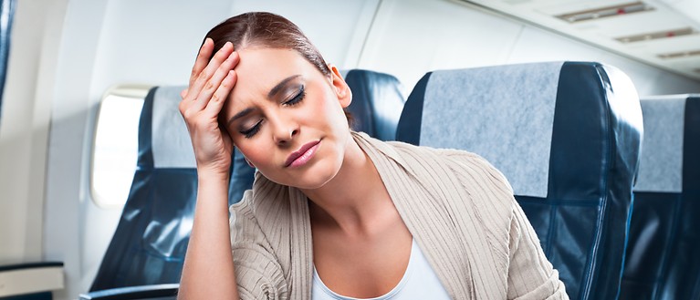 'Eine Frau sitzt im Flugzeug und hält mit ihrer Hand ihren Kopf. 