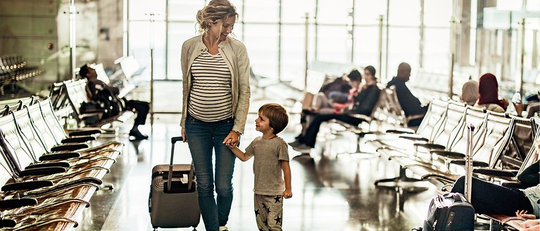 Eine schwangere Frau hält an ihren einen Hand ein Kind und der anderen Hand einen Koffer fest. 