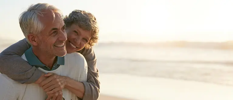 Ein älteres Paar ist am Strand. Beide lächeln.