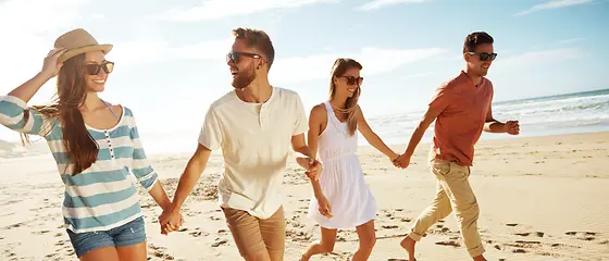 Zwei Pärchen gehen am Strand spazieren und halten Händchen. 